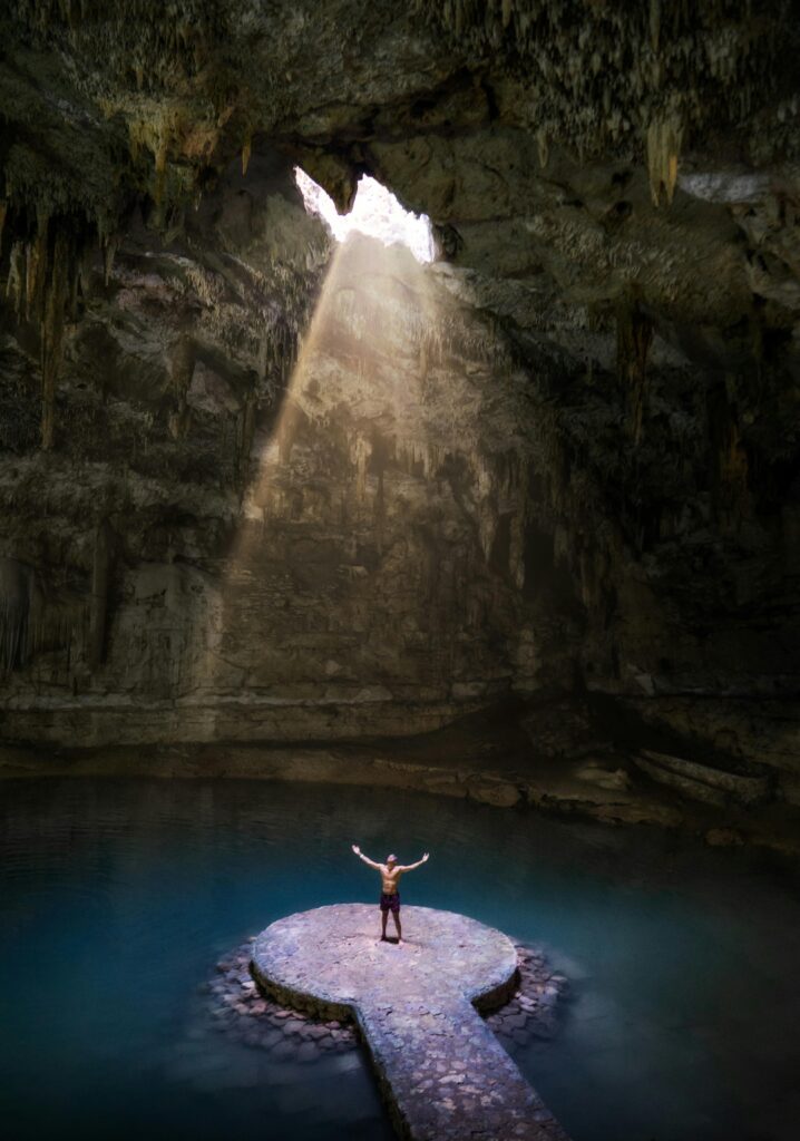 A striking sunbeam illuminates the Suytun Cenote as a person stands in the center. Valladolid, Mexico.